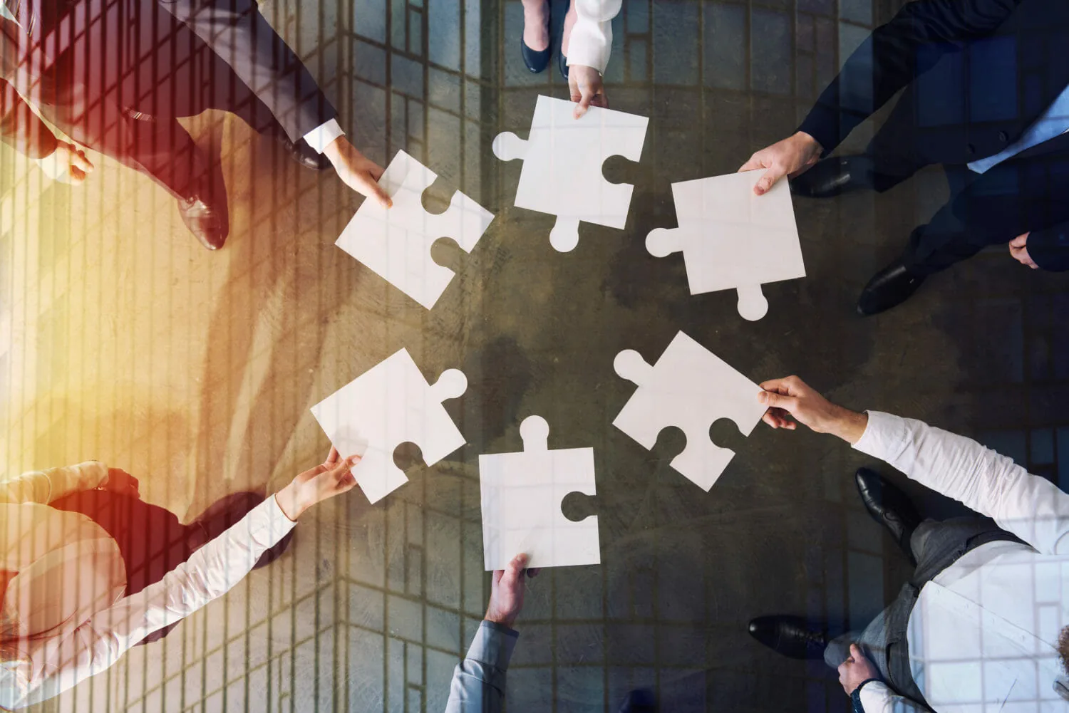 Several people’s hands fitting puzzle pieces together, photographed from above